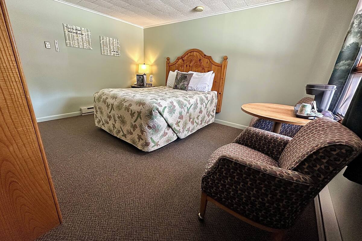 Una habitación de hotel con una cama, una silla, una mesita y una lámpara fijada a la pared.
