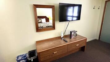 A hotel room with a wooden dresser, a flat-screen TV mounted on the wall, a mirror, and a trash bin.