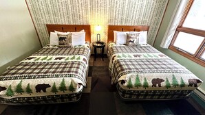 Habitación con dos camas, cada una con colcha de motivos forestales. Hay una mesita entre las camas y una ventana en el lado derecho.