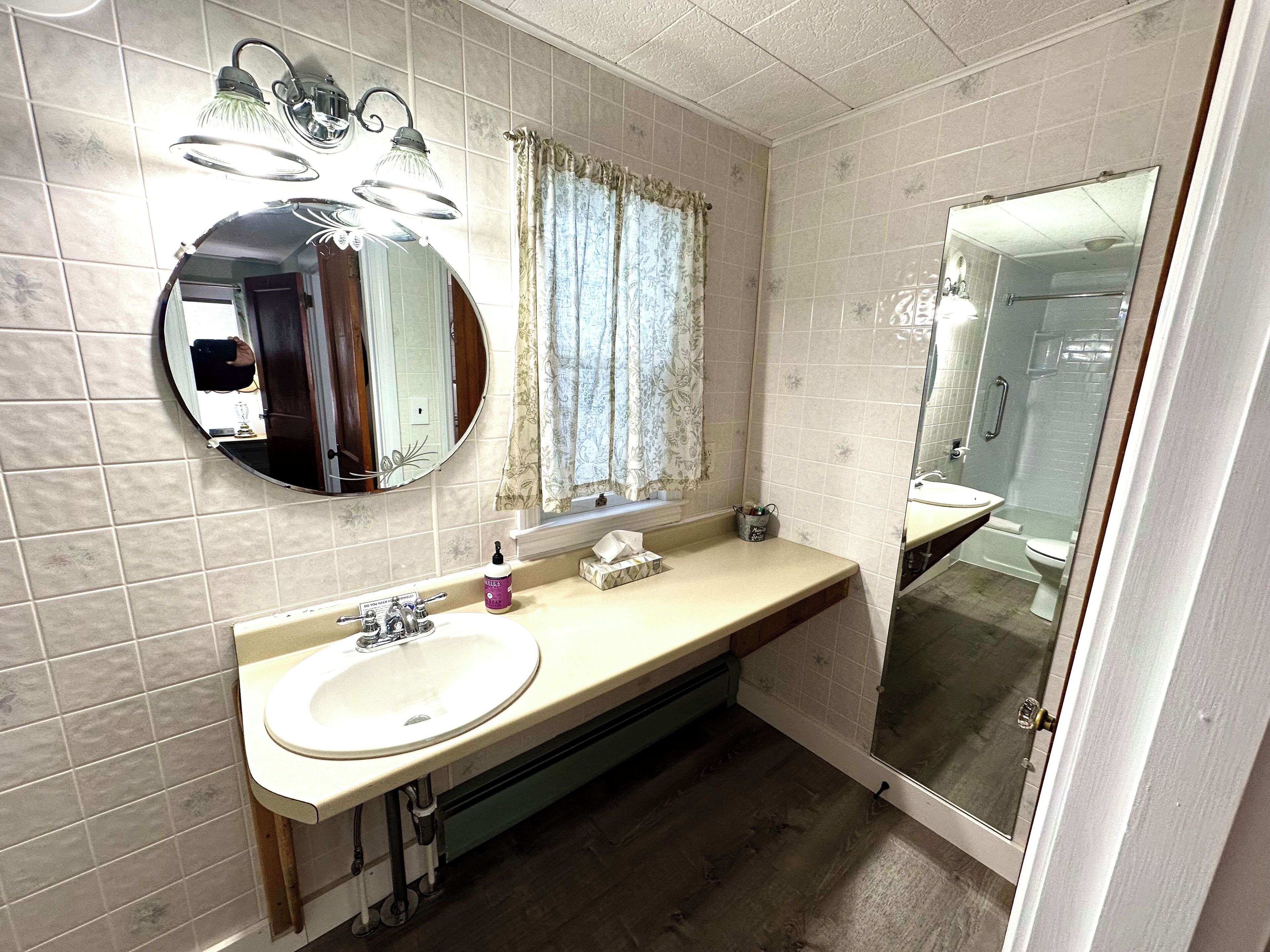A bathroom with a round mirror, a sink, a vanity, a shower, and a toilet.