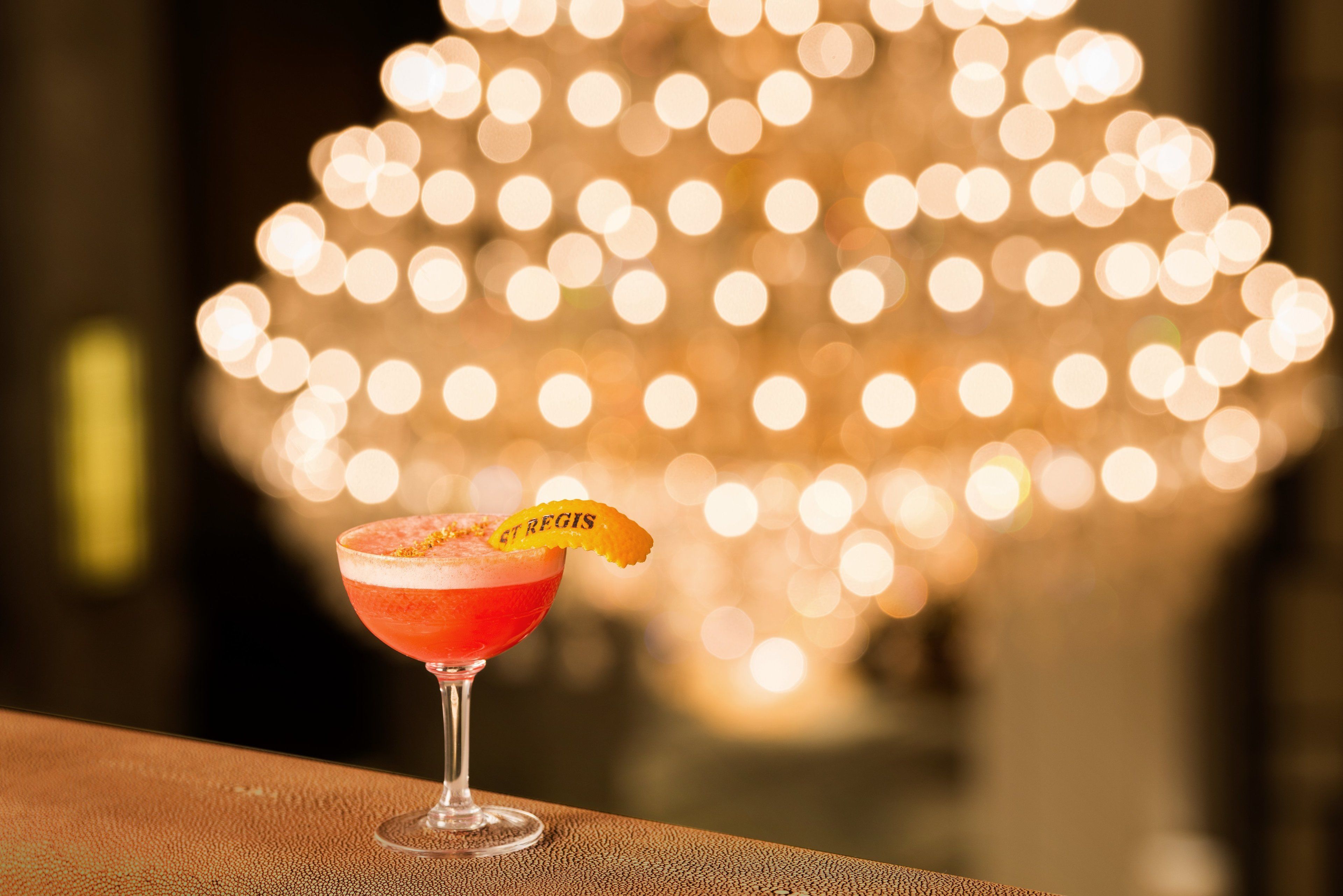 Un cocktail servi dans un verre, agrémenté d’une garniture, sur fond flou de lumières.