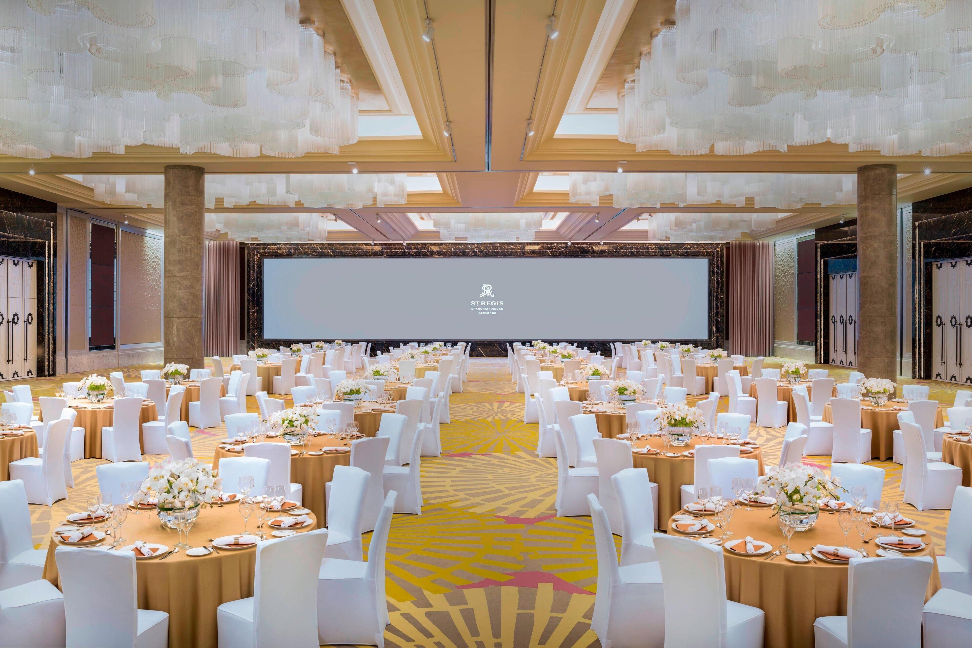 A large conference room with rows of round tables, white chairs, and a stage at the front.