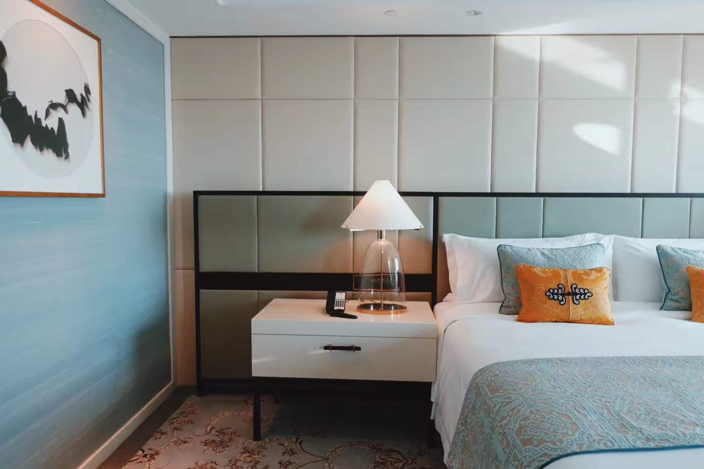A hotel room with a bed, nightstand, lamp, and a framed picture on the wall.