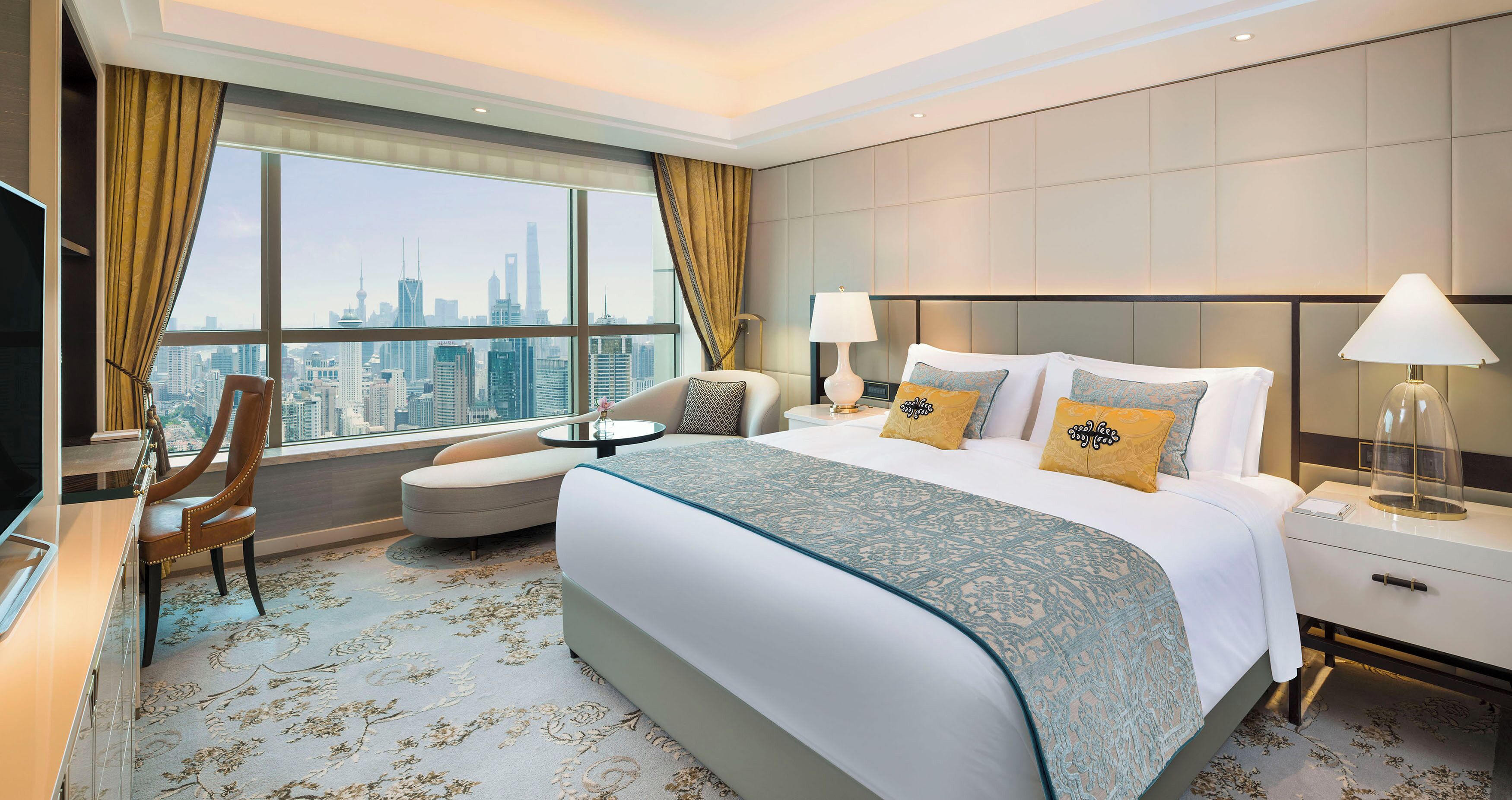 A hotel room with a large bed, a sofa, a chair, a desk, and a view of a city skyline.