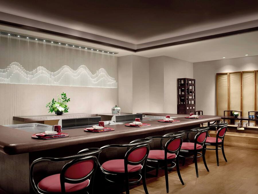 A modern dining area with a long table, red chairs, and a decorative wall feature.