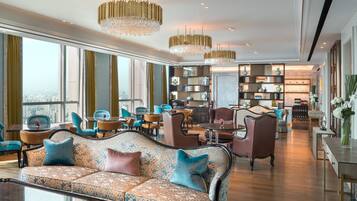 Un amplio lobby de hotel con una gran zona de estar, ambiente luminoso y vistas a la ciudad a través de amplios ventanales.