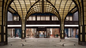 Une entrée imposante avec une façade en verre, une enseigne bien visible indiquant « ST REGIS », et un vaste espace carrelé.