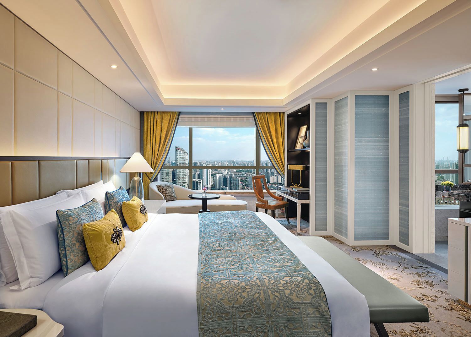 A hotel room with a large bed, a desk, a chair, and a view of the city.