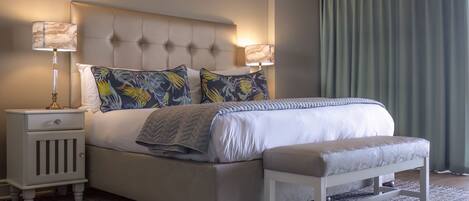 A neatly made bed with a tufted headboard, two decorative pillows, a bedside table with a lamp, and a bench.