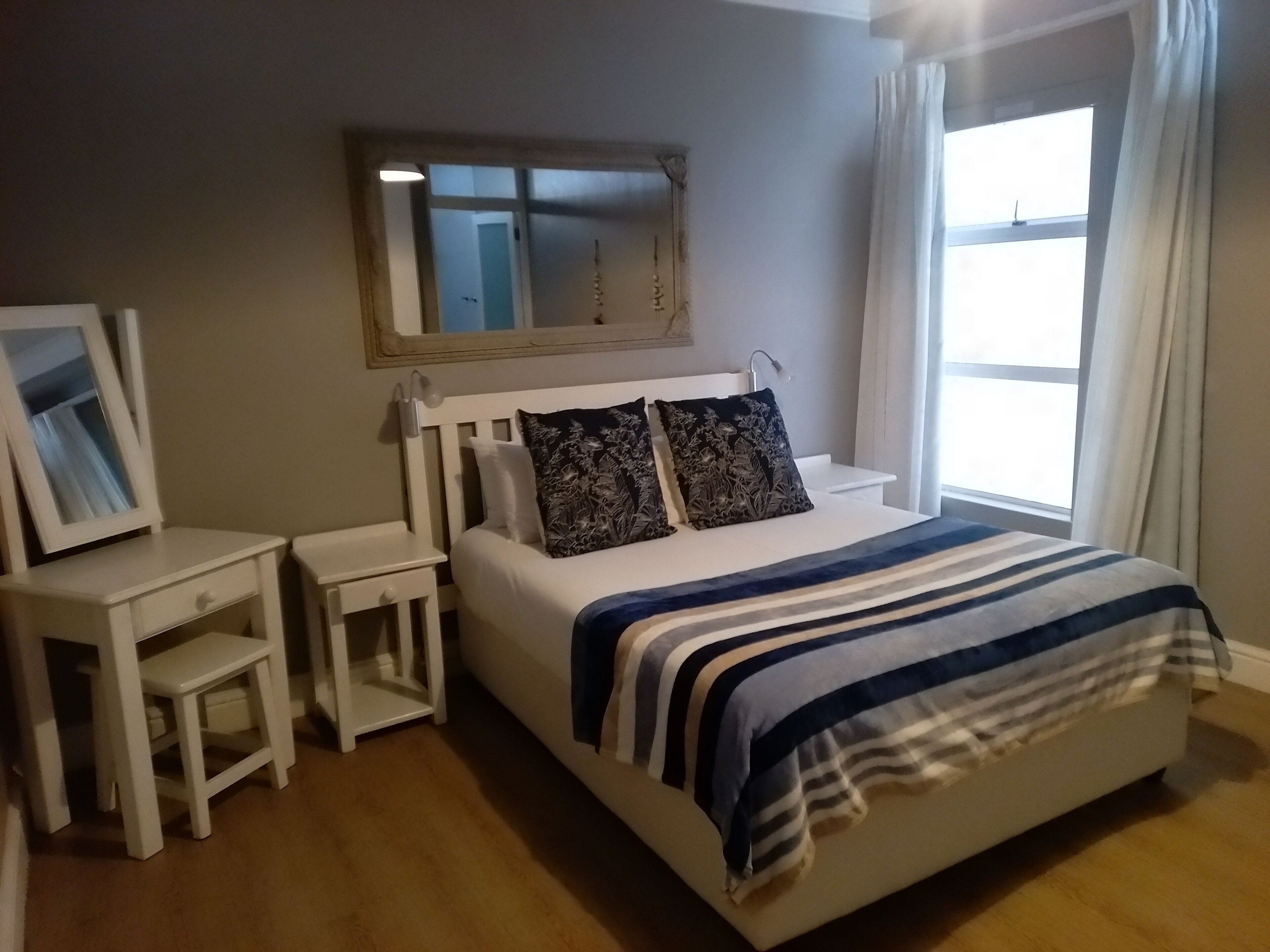 Un dormitorio con cama, mesitas de noche, un espejo y una ventana con cortinas.