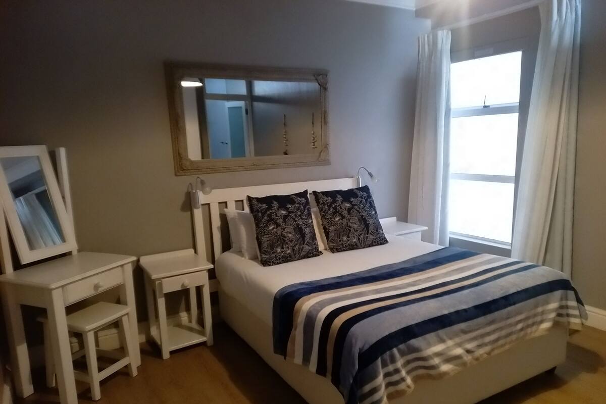 Une chambre à coucher avec un lit, des tables de chevet, un miroir et une fenêtre avec des rideaux.