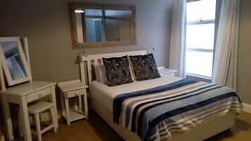 Quarto com cama, mesas de cabeceira, espelho e janela com cortinas.