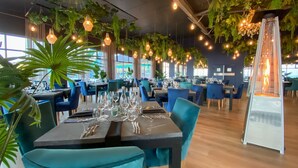 A restaurant with tables set for dining, hanging plants, and pendant lighting. - Diaz Hotel & Resort (Mossel Bay)