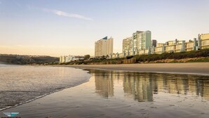 A beach with a sandy shore and a row of buildings in the background. - Diaz Hotel & Resort (Mossel Bay)