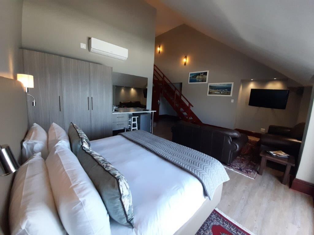 A modern bedroom with a large bed, a desk, a chair, a TV, and a staircase.