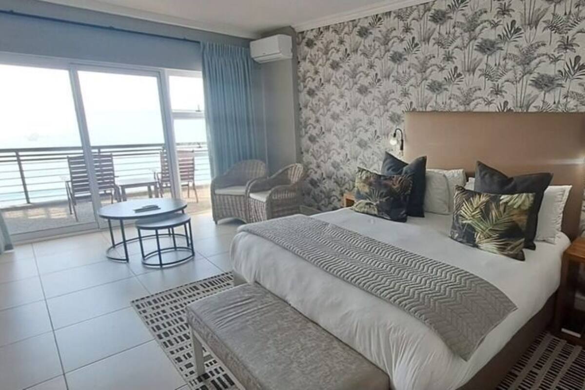 Une chambre d’hôtel avec un grand lit, une petite table, une chaise et une vue sur la mer grâce à de grandes fenêtres.