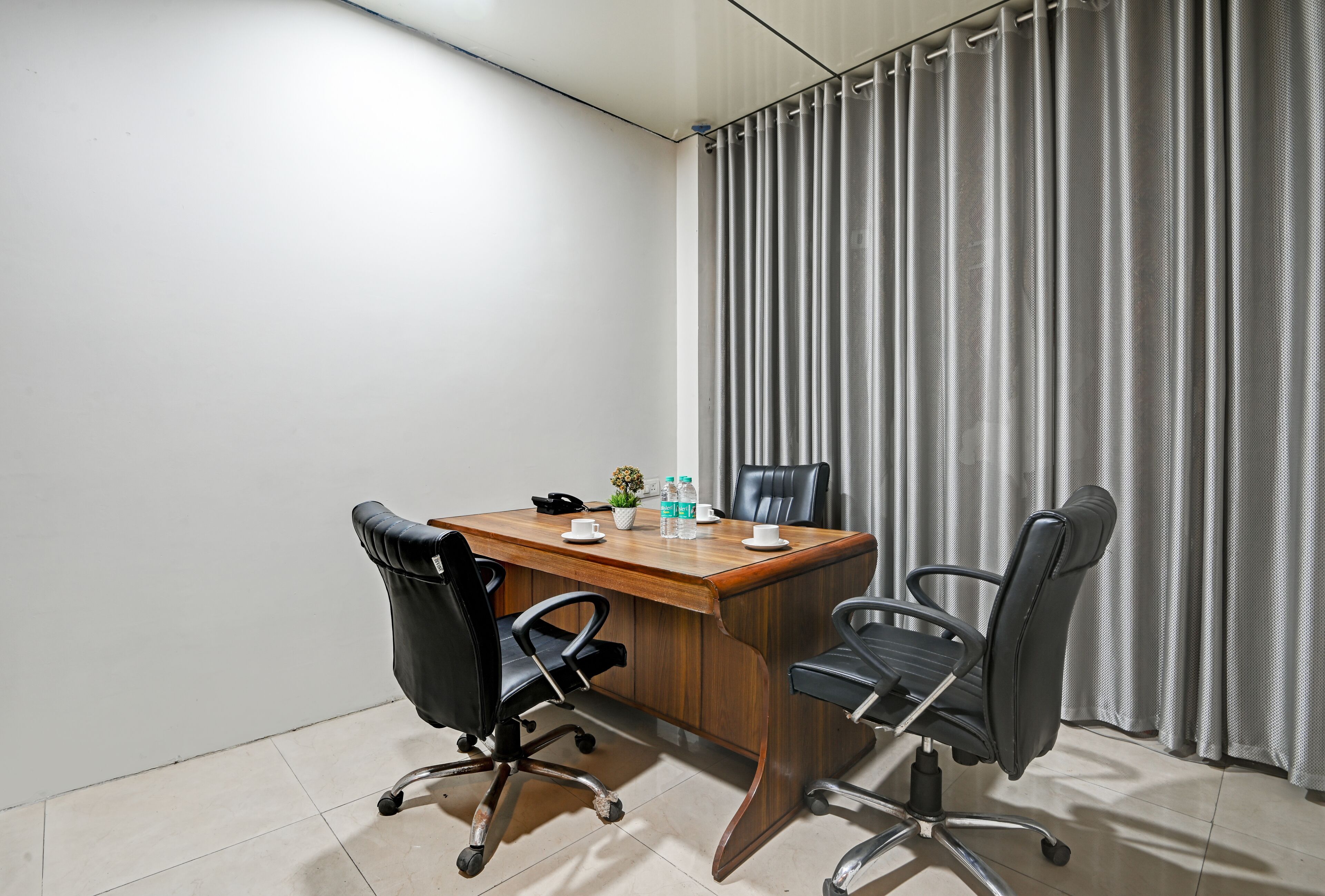 A conference room with a wooden table, two black office chairs, a telephone, and a small potted plant.