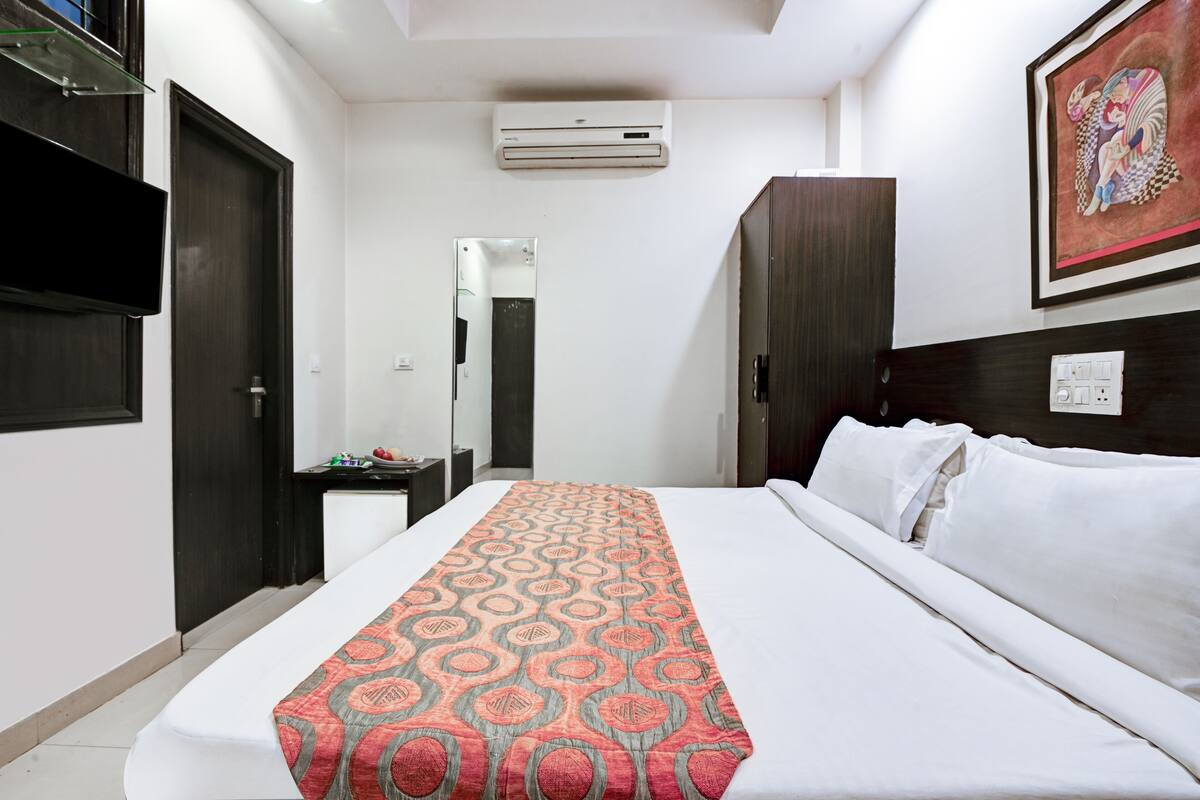 Habitación de hotel con cama, televisor, aire acondicionado, armario y un cuadro en la pared.