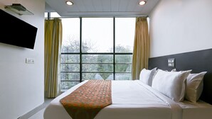 A hotel room with a large bed, a flat-screen TV mounted on the wall, and a window with curtains.