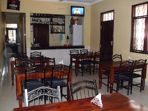 A restaurant with wooden tables and chairs, a bar area with various bottles, and a television screen.