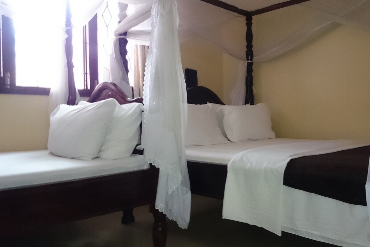 A room with a bed under a canopy, a bedside table, and a window with curtains.
