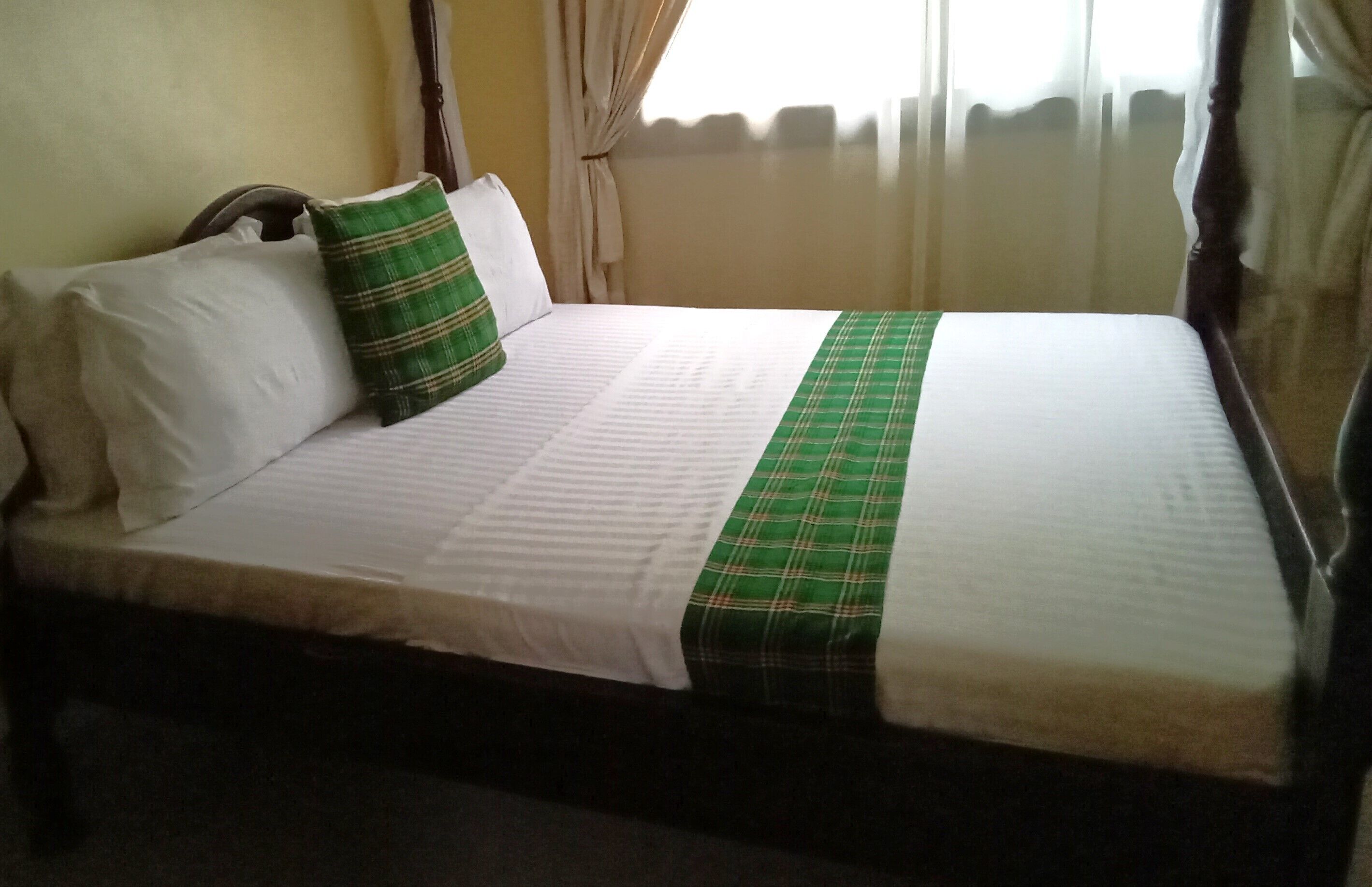 A neatly made bed with white and green striped bedding, a wooden headboard, and a window with curtains.