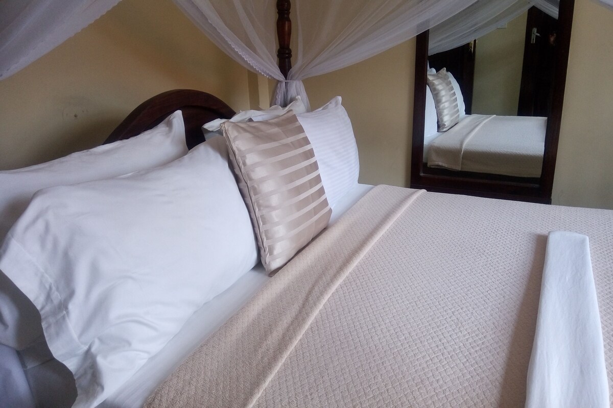 A neatly made bed with white and beige pillows, a textured white bedspread, and a canopy overhead.