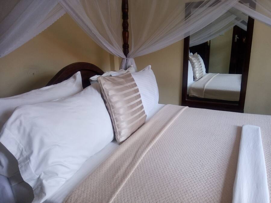 A neatly made bed with white and beige pillows, a textured white bedspread, and a canopy overhead.