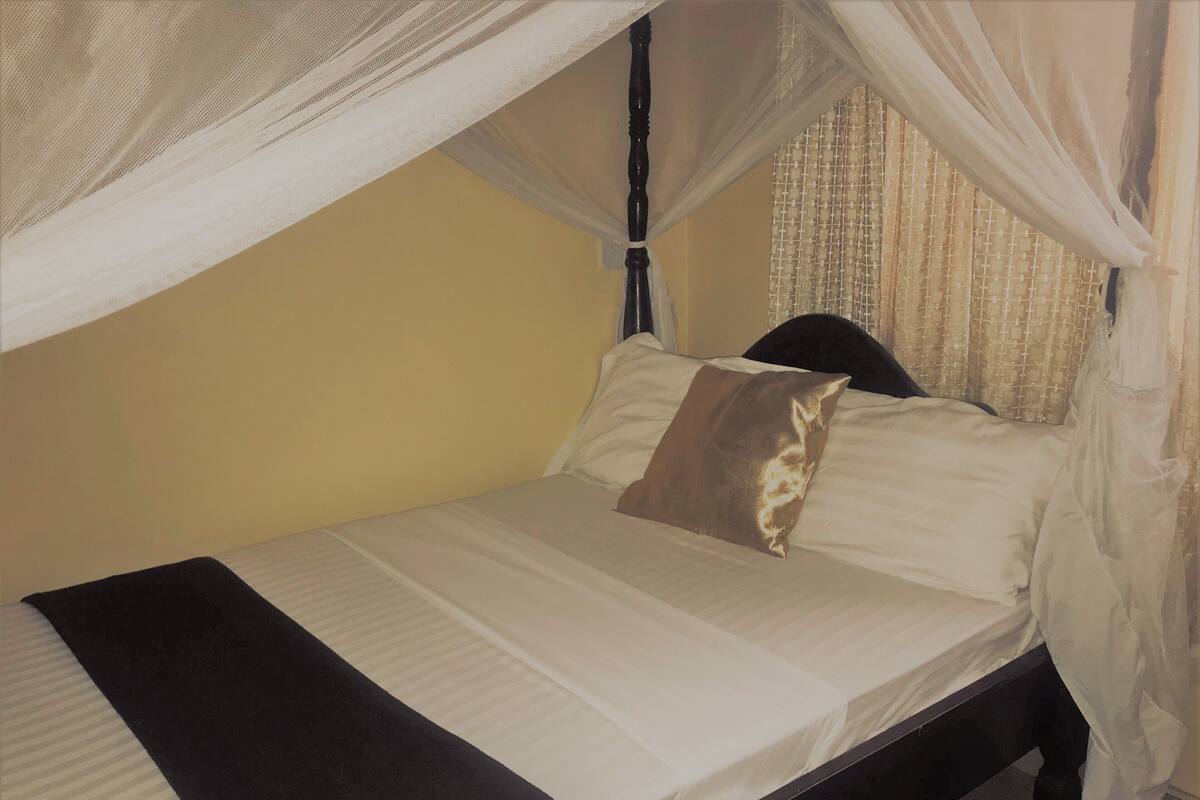 A bed with a canopy, white linens, and a brown pillow.