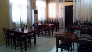 A dining area with wooden tables and chairs, white curtains, and a ceiling fan.