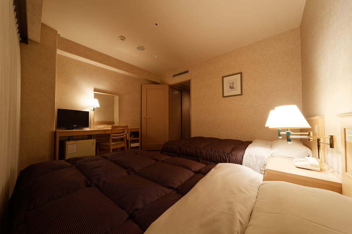 Ein Hotelzimmer mit einem Bett, einem Schreibtisch mit Computer, einem Stuhl und einer Lampe.