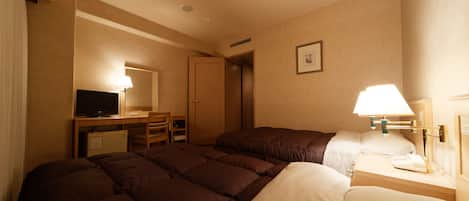 A hotel room with a bed, a desk with a computer, a chair, and a lamp.