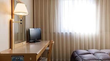 A hotel room with a wooden desk, a television, a mirror, a bed with pillows, and a window with curtains.