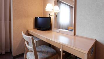 Quarto de hotel com escrivaninha de madeira, televisão, cadeira, espelho e abajur.