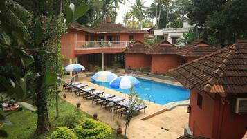Relax by the serene pool surrounded by lush greenery and shaded lounge chairs.