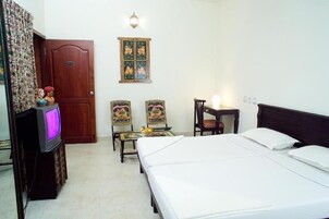 Habitación de hotel con cama, dos sillas, una mesita, televisor, puerta y mueble empotrado.