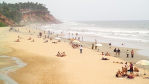 A beach with people sunbathing and walking along the shore.