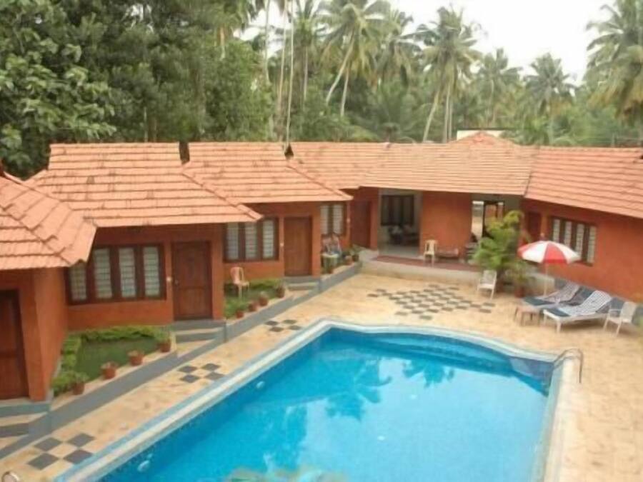 Un espace piscine doté d’une terrasse carrelée, d’une piscine et de plusieurs bâtiments de style bungalow avec des toits rouges.