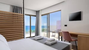 Een hotelkamer met een bed, een bureau, een stoel, een televisie en een balkon met uitzicht op zee.