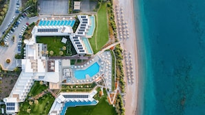 Luchtbeeld van een resort met meerdere zwembaden, een strand en een parkeerplaats.