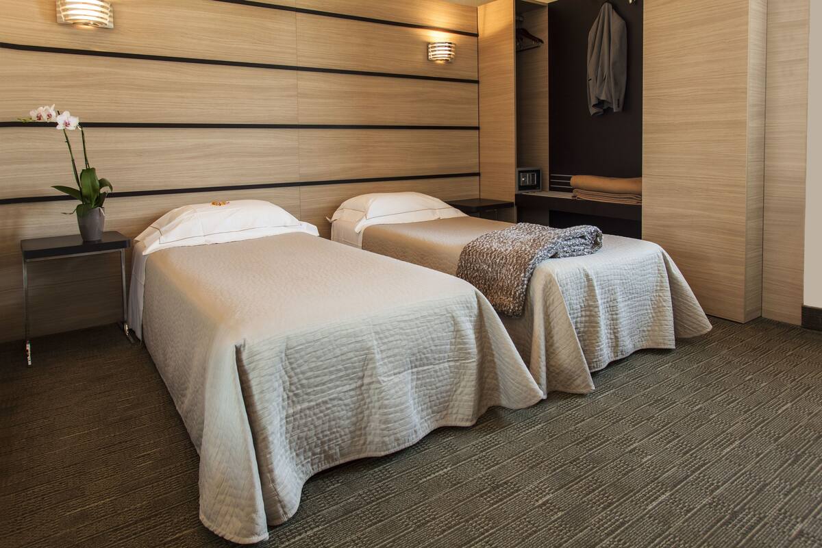 A hotel room with two beds, a nightstand with a vase of flowers, a mirror, and a coat rack.