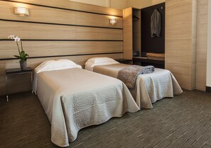 A hotel room with two beds, a nightstand with a vase of flowers, a mirror, and a coat rack.