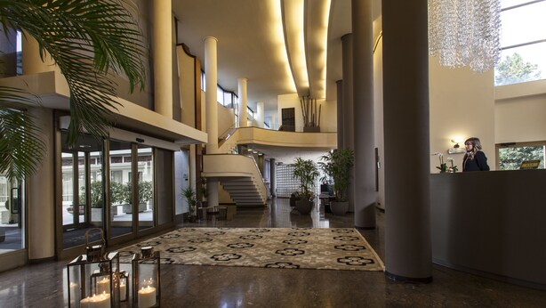 Un amplio vestíbulo con una escalera central, grandes columnas y un mostrador de recepción.