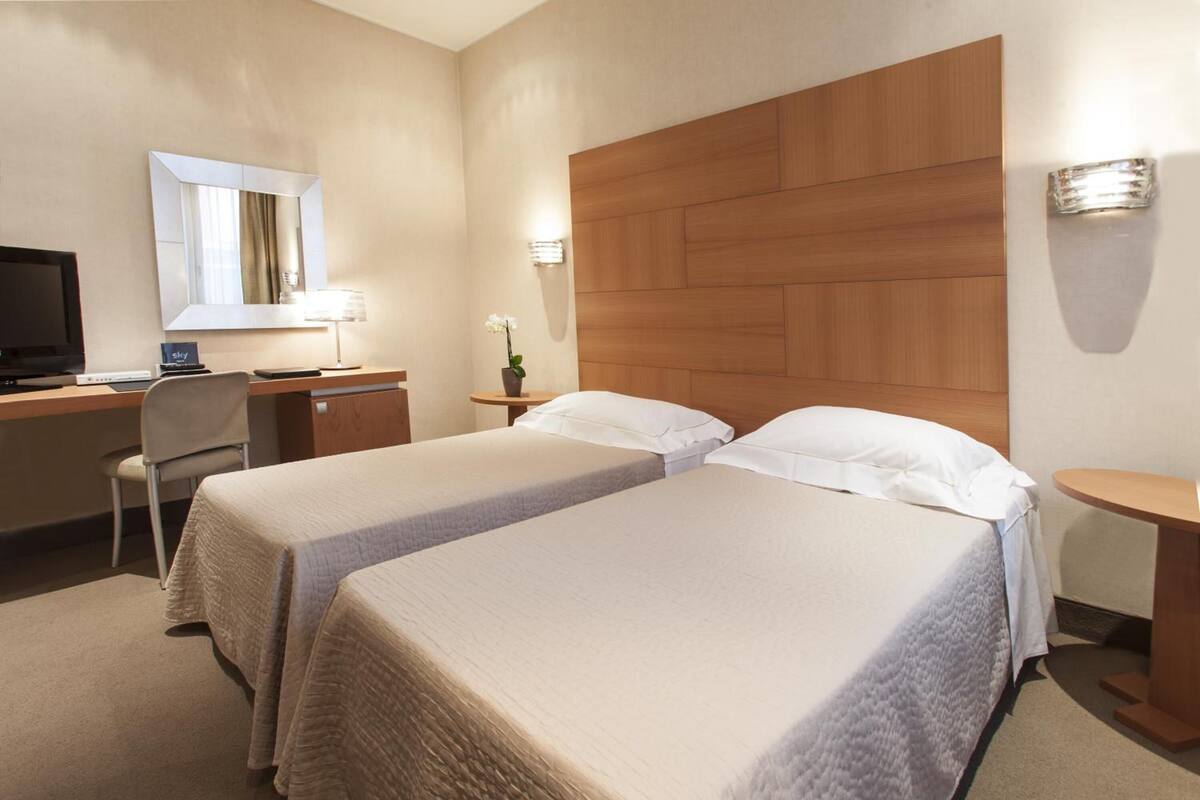 A hotel room with two beds, a desk with a computer, a TV, and a mirror.