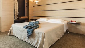 Habitación de hotel con una cama grande, una mesita de noche con una bandeja de frutas y una lámpara fijada a la pared.