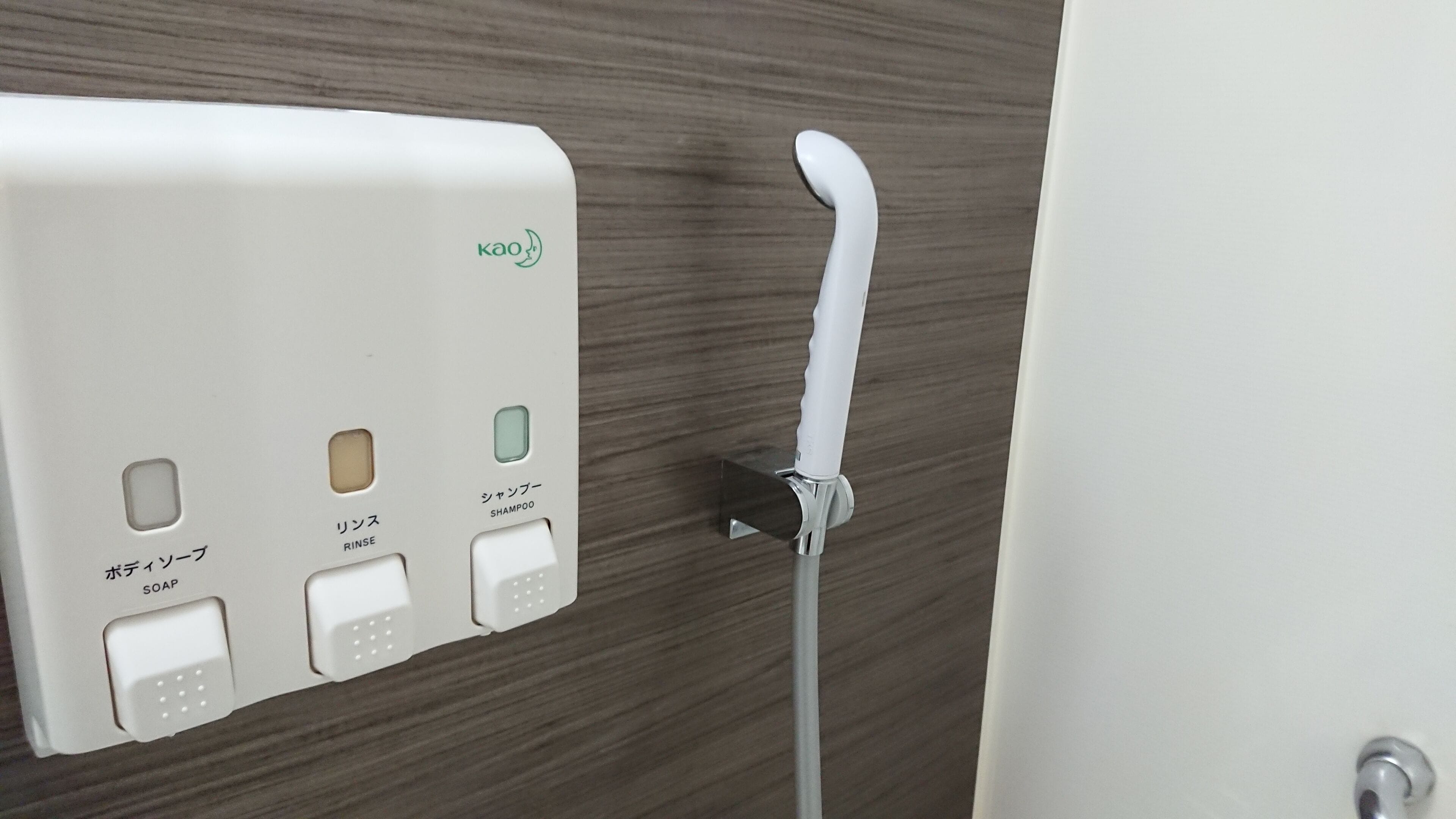 A bathroom with a soap dispenser, rinse, and shampoo dispenser mounted on a wall.