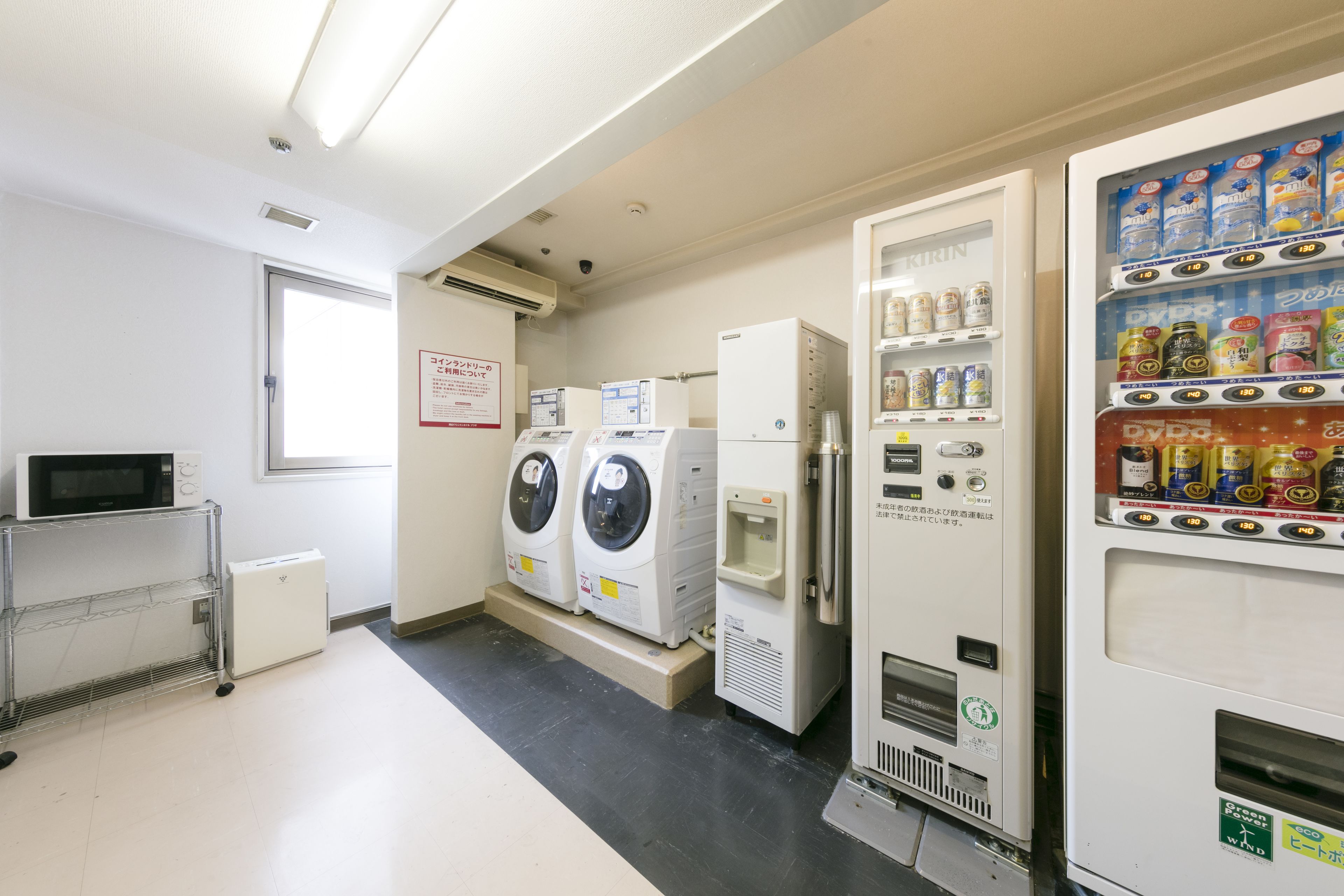 A laundry room with a microwave, two washing machines, a refrigerator, and a vending machine.