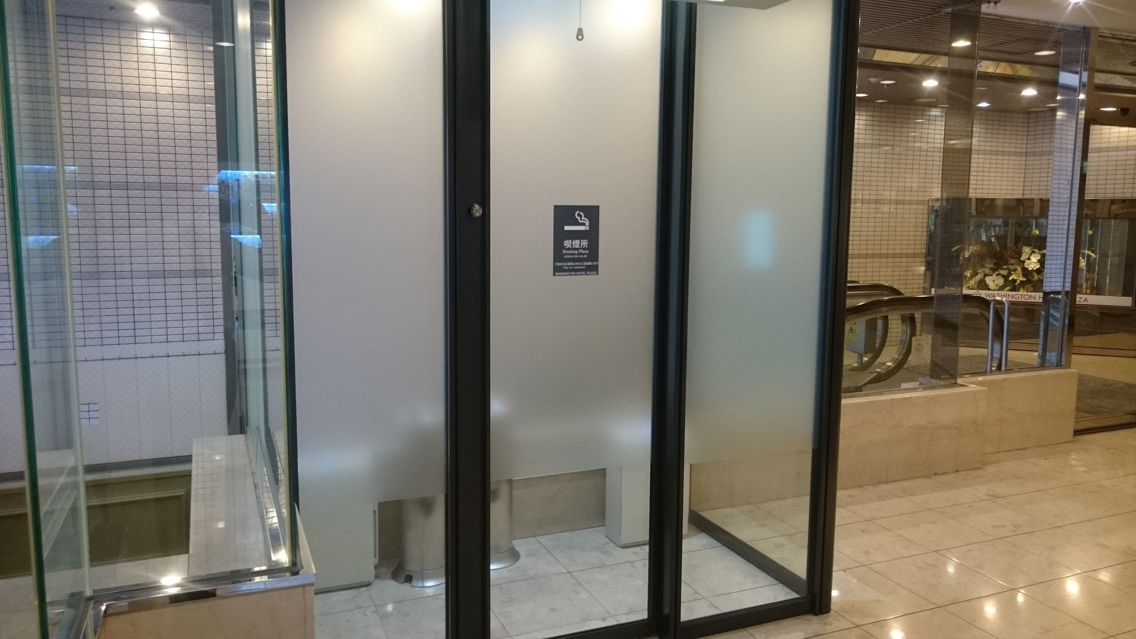 L’entrée d’un hôtel, avec une porte en verre, un panneau indiquant un espace fumeurs et un sol carrelé.