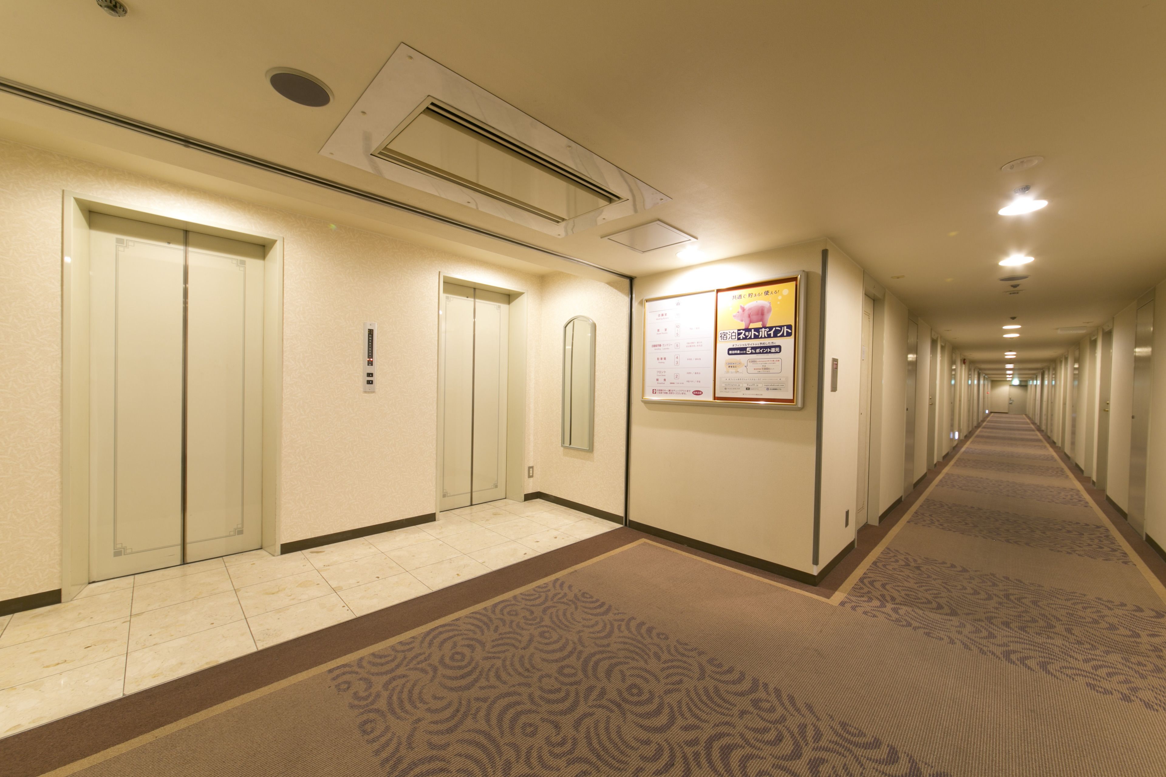 A hotel hallway with carpeted floors, doors, and a poster on the wall.