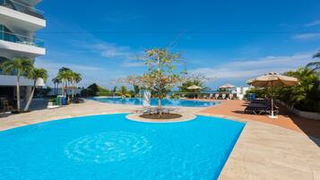 A large swimming pool with a circular design, surrounded by palm trees and lounge chairs.